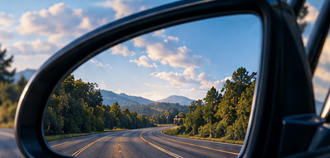 Side mirror reflecting a tree-lined highway under a blue sky